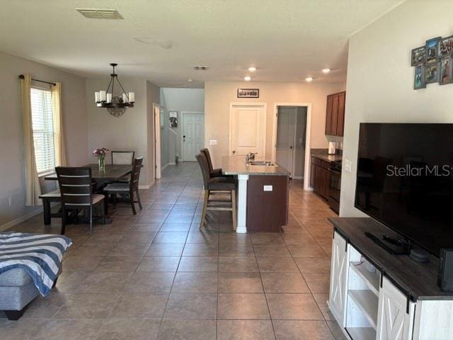 kitchen with a notable chandelier, a breakfast bar, visible vents, a sink, and a center island with sink