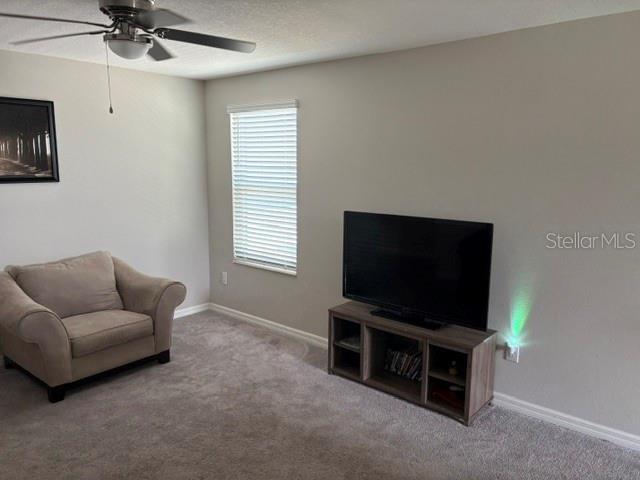carpeted living area featuring baseboards and ceiling fan