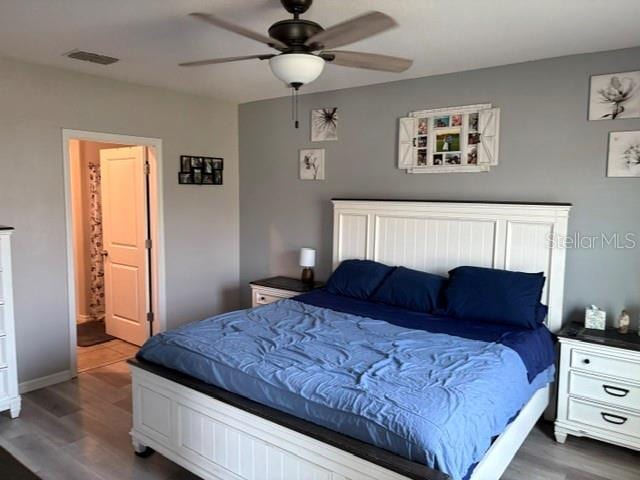 bedroom featuring ensuite bathroom, a ceiling fan, visible vents, and wood finished floors