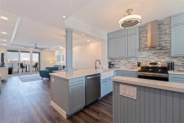 kitchen with appliances with stainless steel finishes, a sink, wall chimney exhaust hood, decorative columns, and gray cabinets