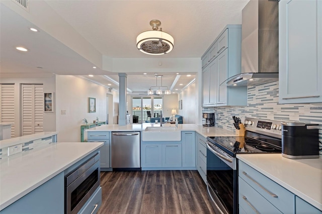 kitchen featuring stainless steel appliances, a sink, wall chimney range hood, dark wood-type flooring, and light countertops