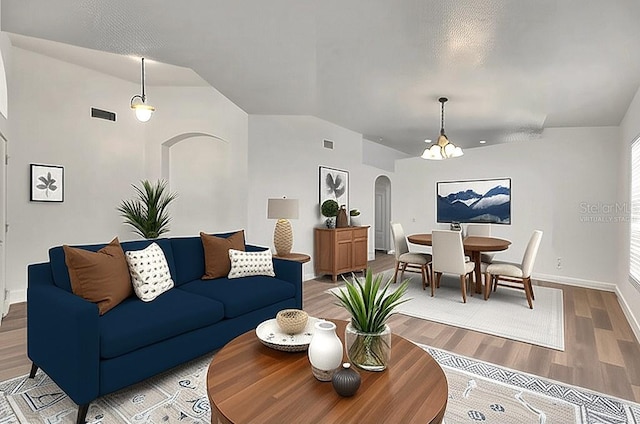 living area with arched walkways, light wood-style flooring, baseboards, and lofted ceiling