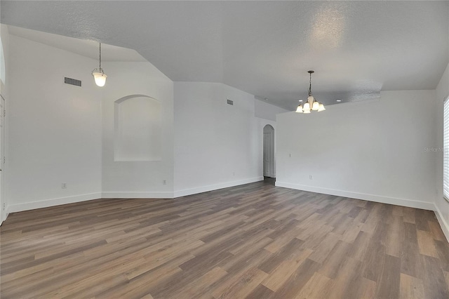 unfurnished room featuring a chandelier, arched walkways, wood finished floors, baseboards, and vaulted ceiling