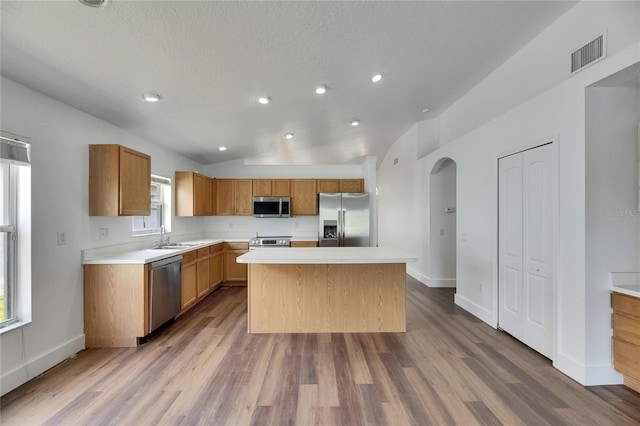 kitchen with appliances with stainless steel finishes, light countertops, wood finished floors, a sink, and a center island
