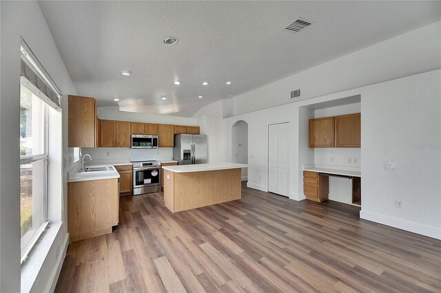 kitchen with stainless steel appliances, lofted ceiling, a kitchen island, arched walkways, and a sink