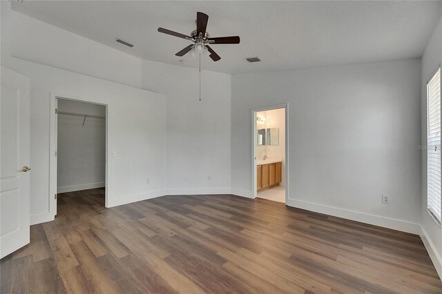 unfurnished bedroom with a walk in closet, wood finished floors, baseboards, and ensuite bath