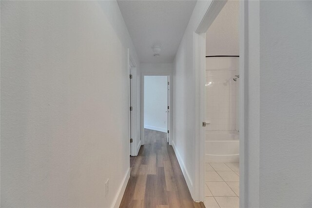 hallway featuring wood finished floors, baseboards, and a textured wall