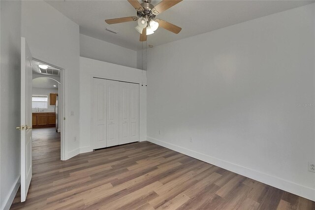 unfurnished bedroom featuring wood finished floors, baseboards, arched walkways, and a closet