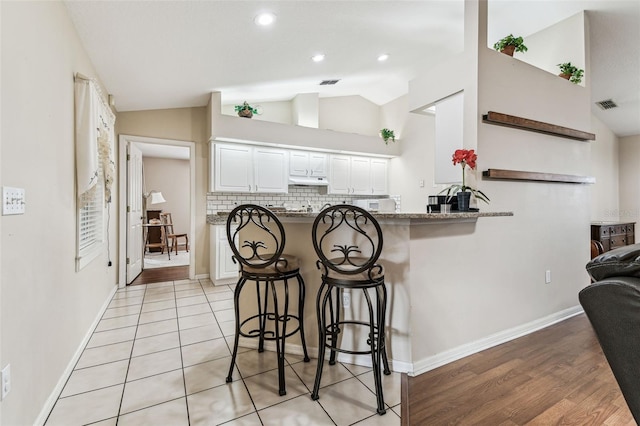 1202 Williams Rd, Plant City, FL 33565 - kitchen featuring vaulted ceiling, a breakfast bar, decorative backsplash, white cabinets, and baseboards
