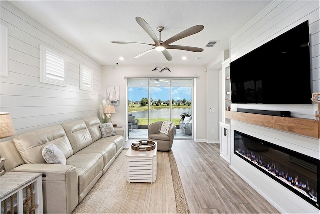 10418 Spring Tide Way, Parrish, FL 34219 - living area featuring a glass covered fireplace, ceiling fan, light wood finished floors, wood walls, and recessed lighting