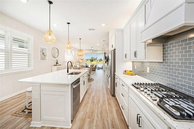 10418 Spring Tide Way, Parrish, FL 34219 - kitchen with premium range hood, stainless steel appliances, a sink, open floor plan, and light wood-style flooring