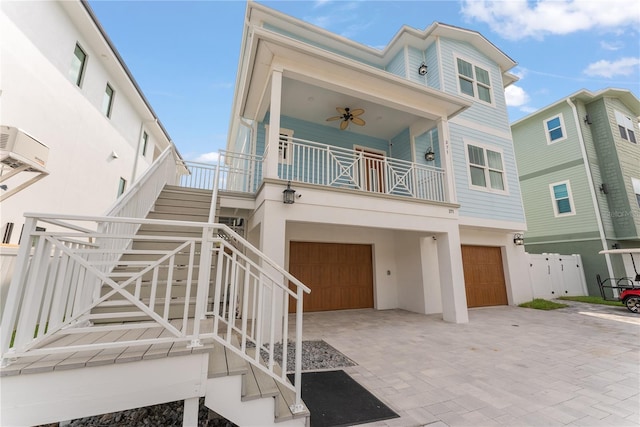 coastal home with an attached garage, ceiling fan, stairs, stucco siding, and driveway