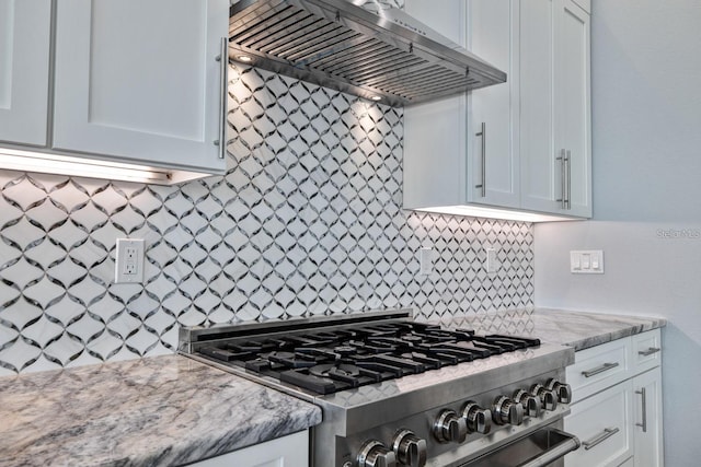 kitchen with gas range, range hood, decorative backsplash, white cabinets, and light stone counters