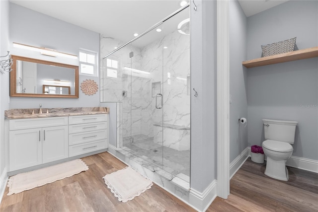 bathroom featuring toilet, wood finished floors, vanity, a marble finish shower, and baseboards