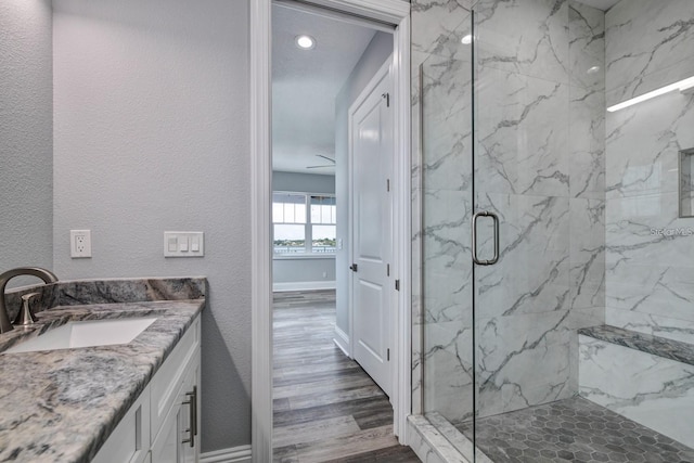 bathroom featuring a marble finish shower, wood finished floors, vanity, recessed lighting, and baseboards