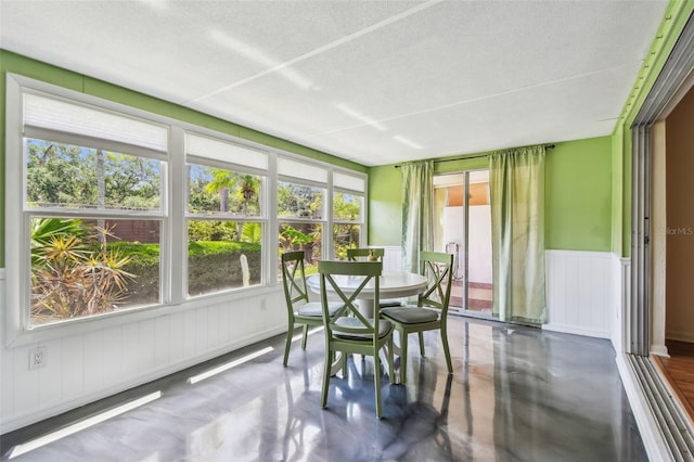 sunroom / solarium featuring plenty of natural light, a textured ceiling, wainscoting, finished concrete flooring, and a decorative wall