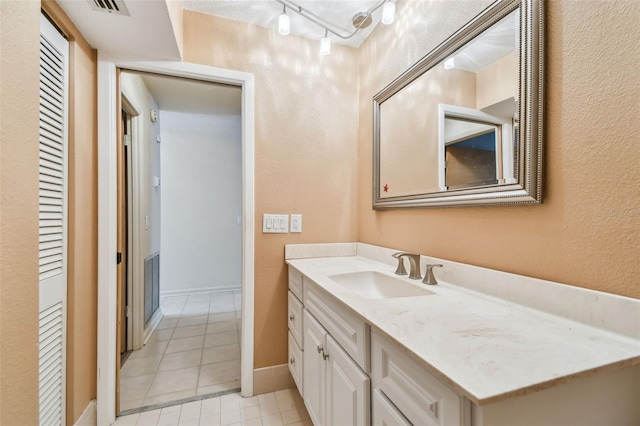 bathroom with tile patterned flooring, vanity, a textured wall, rail lighting, and baseboards