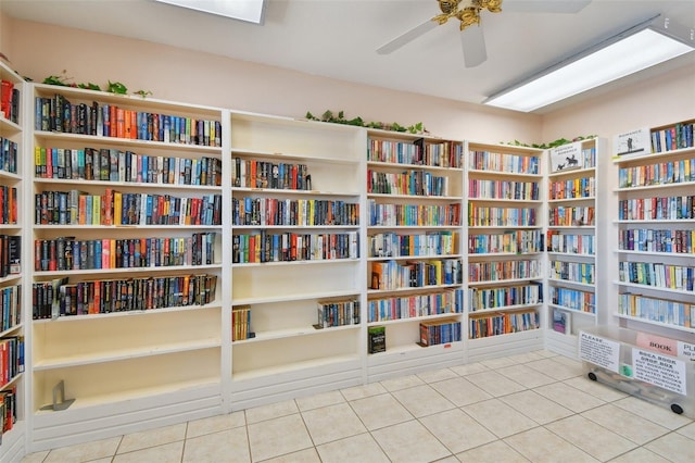 living area with wall of books, tile patterned flooring, and ceiling fan
