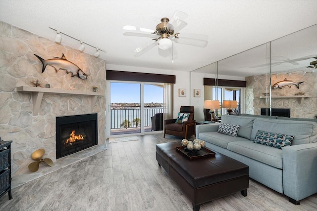 living area featuring ceiling fan, rail lighting, wood finished floors, and a stone fireplace