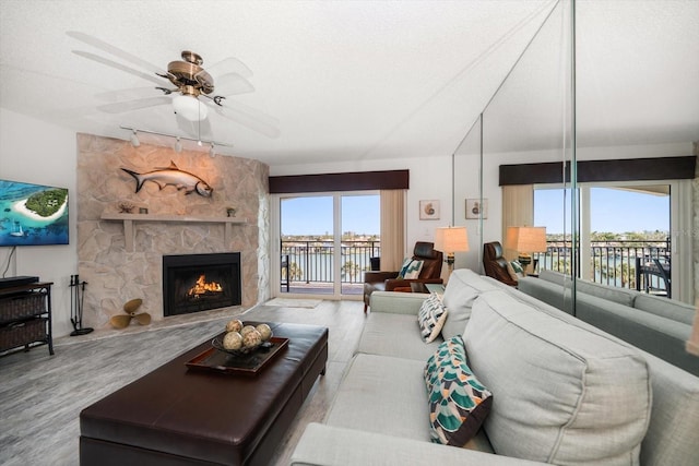 living area featuring track lighting, a water view, wood finished floors, and a stone fireplace
