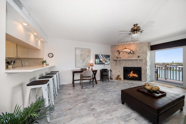 living area featuring a textured ceiling, a ceiling fan, a stone fireplace, and recessed lighting
