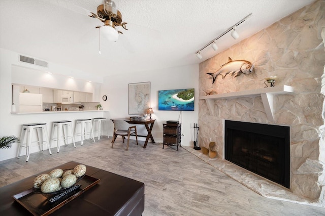 living area with wood finished floors, rail lighting, a textured ceiling, visible vents, and a stone fireplace