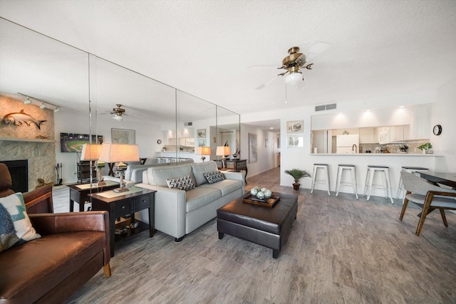 living room featuring a ceiling fan, a stone fireplace, visible vents, and wood finished floors