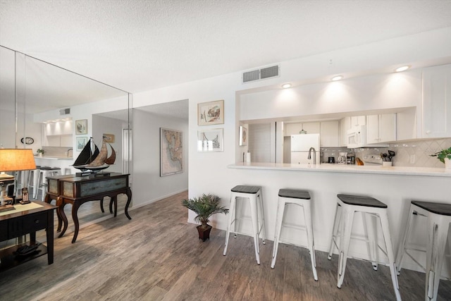 kitchen featuring white appliances, a breakfast bar, visible vents, backsplash, and light countertops