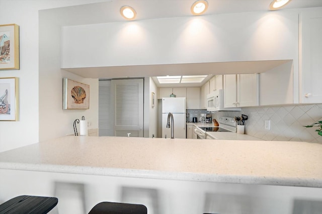 kitchen with a peninsula, white appliances, a breakfast bar, decorative backsplash, and light stone countertops