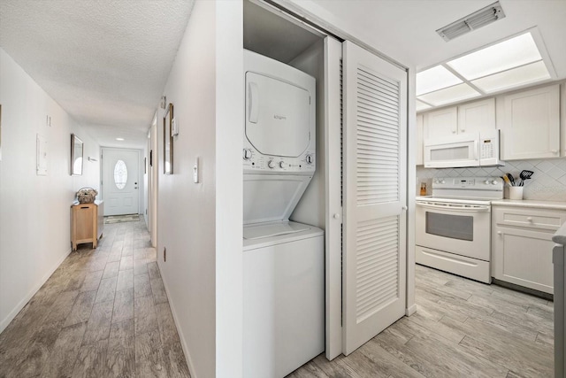 laundry room with laundry area, stacked washer / drying machine, light wood-type flooring, visible vents, and baseboards