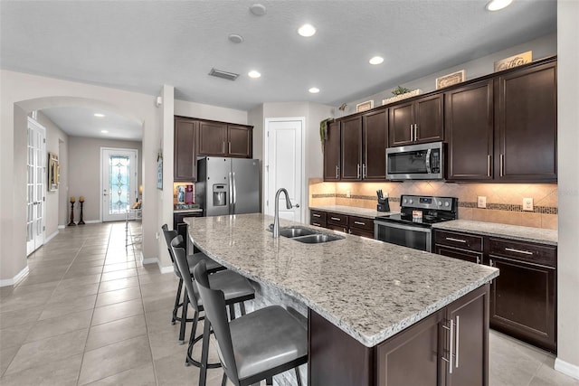 11606 Kilkenny Coral Dr, Riverview, FL 33579 - kitchen featuring stainless steel appliances, arched walkways, a sink, backsplash, and dark brown cabinetry