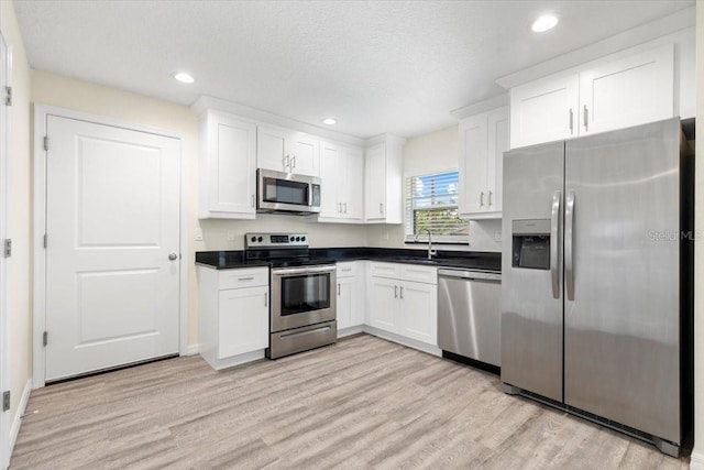 2906 E Columbus Dr, Tampa, FL 33605 - kitchen featuring light wood finished floors, a sink, dark countertops, stainless steel appliances, and white cabinetry