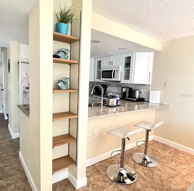 323 Rex Pl Unit G, Madeira Beach, FL 33708 - kitchen featuring white microwave, a textured ceiling, stainless steel range with electric cooktop, white cabinetry, and glass insert cabinets