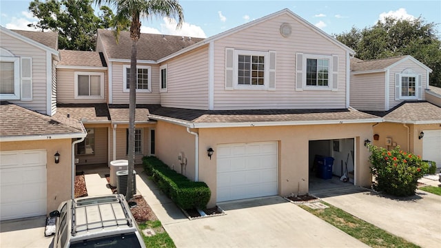 multi unit property featuring concrete driveway, central AC unit, a shingled roof, and an attached garage