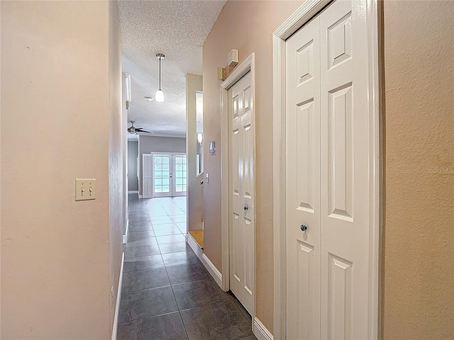 corridor with a textured ceiling, dark tile patterned flooring, baseboards, and a textured wall
