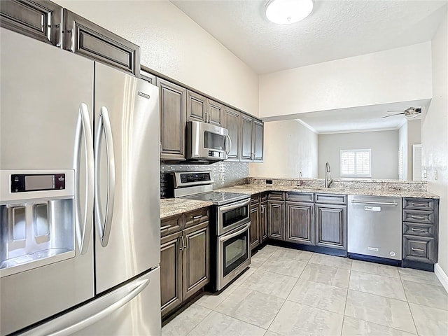 kitchen with a sink, dark brown cabinetry, backsplash, appliances with stainless steel finishes, and light stone counters