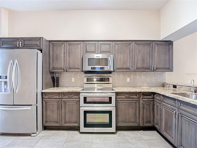 kitchen featuring stainless steel appliances, a sink, tasteful backsplash, and dark brown cabinetry