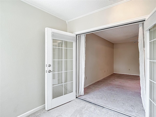 carpeted spare room with ornamental molding, a textured ceiling, baseboards, and french doors