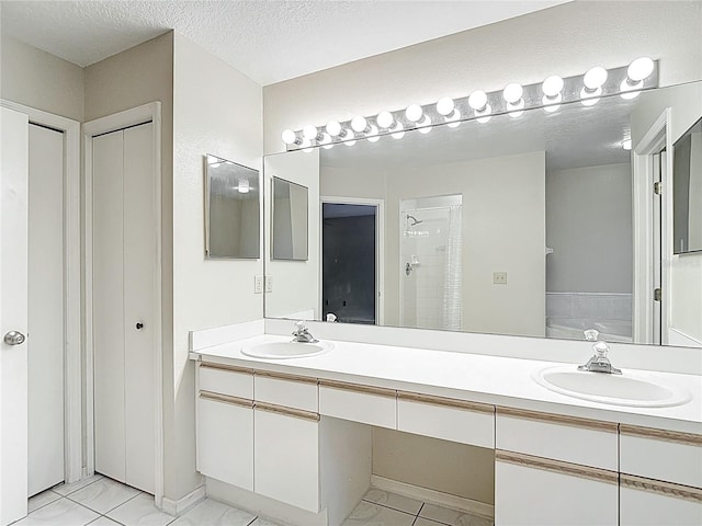 full bath featuring a sink, double vanity, a textured ceiling, and a tile shower
