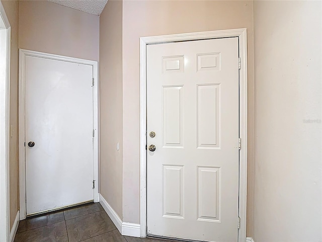 doorway to outside with baseboards and dark tile patterned flooring