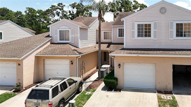 multi unit property with a shingled roof, stucco siding, driveway, and central air condition unit