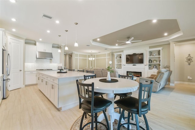 kitchen featuring freestanding refrigerator, a tray ceiling, under cabinet range hood, a ceiling fan, and a center island