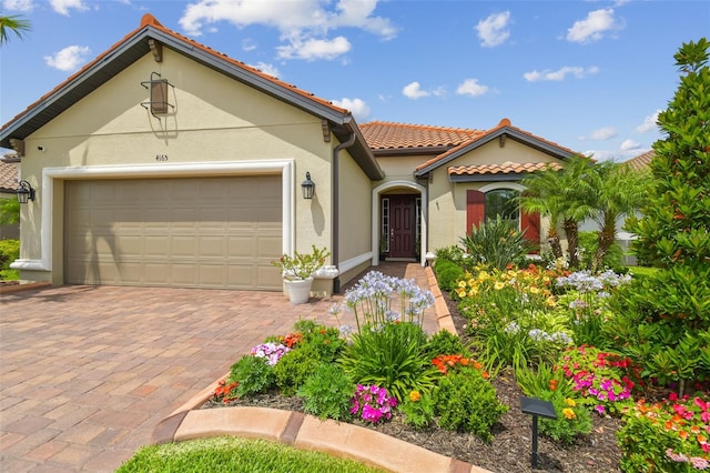 mediterranean / spanish house with a tile roof, stucco siding, a garage, and decorative driveway