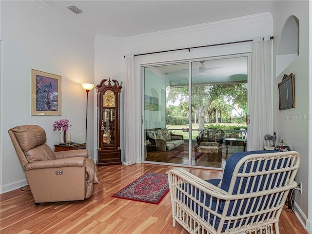 living room with a ceiling fan, baseboards, visible vents, crown molding, and wood finished floors