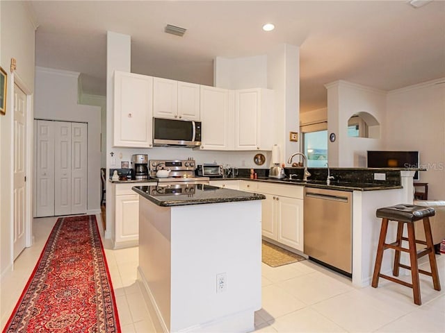 kitchen with a peninsula, appliances with stainless steel finishes, a center island, and white cabinets