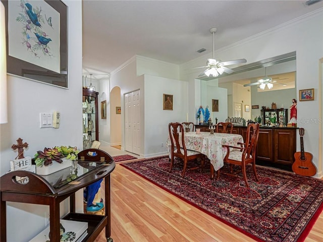 dining area featuring arched walkways, ceiling fan, crown molding, and wood finished floors