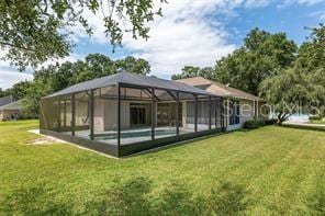 rear view of property featuring a lawn, an outdoor pool, and glass enclosure