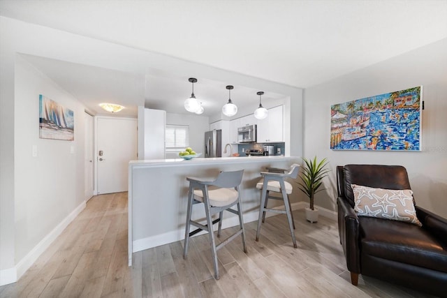 868 Bayway Blvd Unit 206, Clearwater Beach, FL 33767 - kitchen with stainless steel appliances, white cabinetry, light wood-type flooring, and a kitchen bar