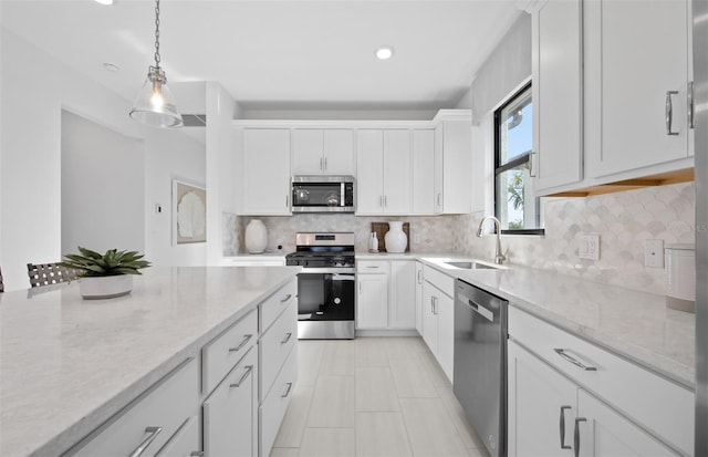 kitchen featuring appliances with stainless steel finishes, a sink, light stone counters, white cabinetry, and pendant lighting