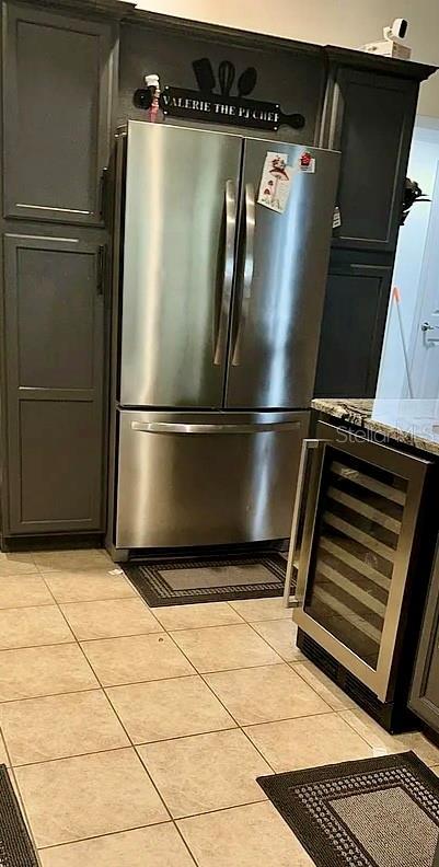 1030 Marcello Blvd, Kissimmee, FL 34746 - details featuring freestanding refrigerator, light stone counters, dark cabinetry, and wine cooler